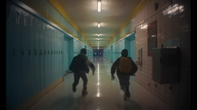 two people walking down a long hallway with lockers