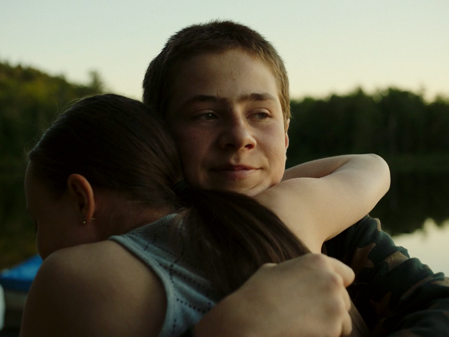 a boy and a girl hugging each other in front of a body of water