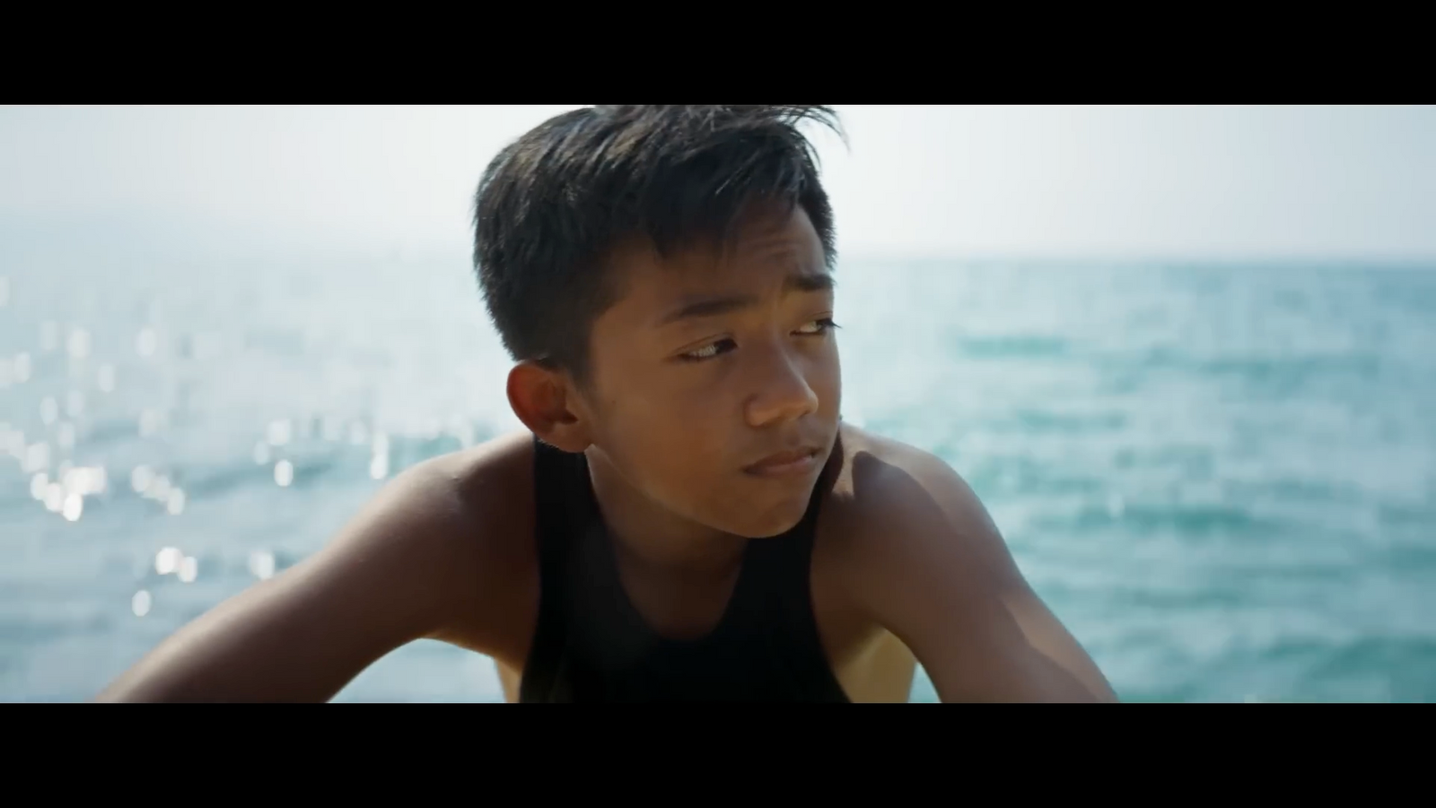 a young boy sitting on a beach next to the ocean