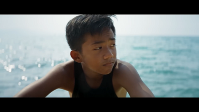 a young boy sitting on a beach next to the ocean