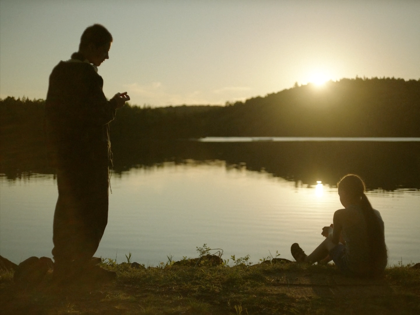 a man and a woman sitting on the ground next to a lake