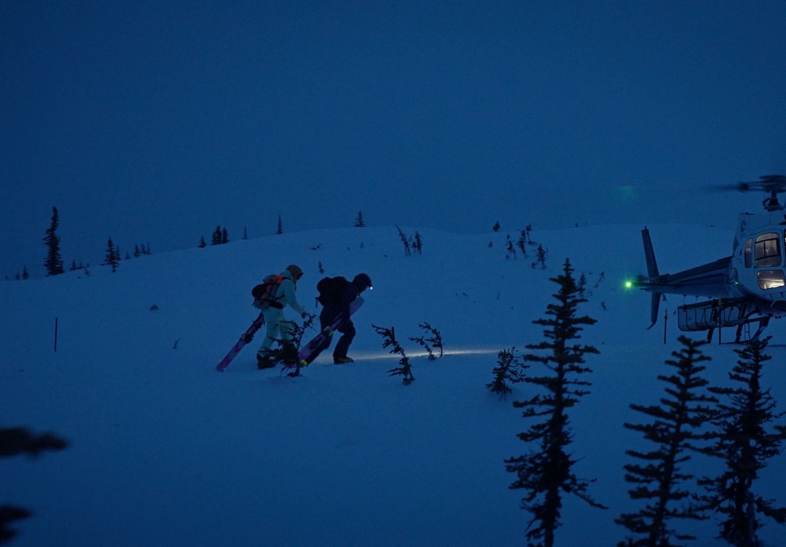 two people walking up a snow covered hill with a helicopter in the background