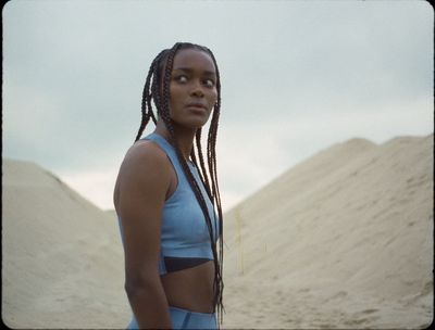 a woman standing in the sand wearing a blue top