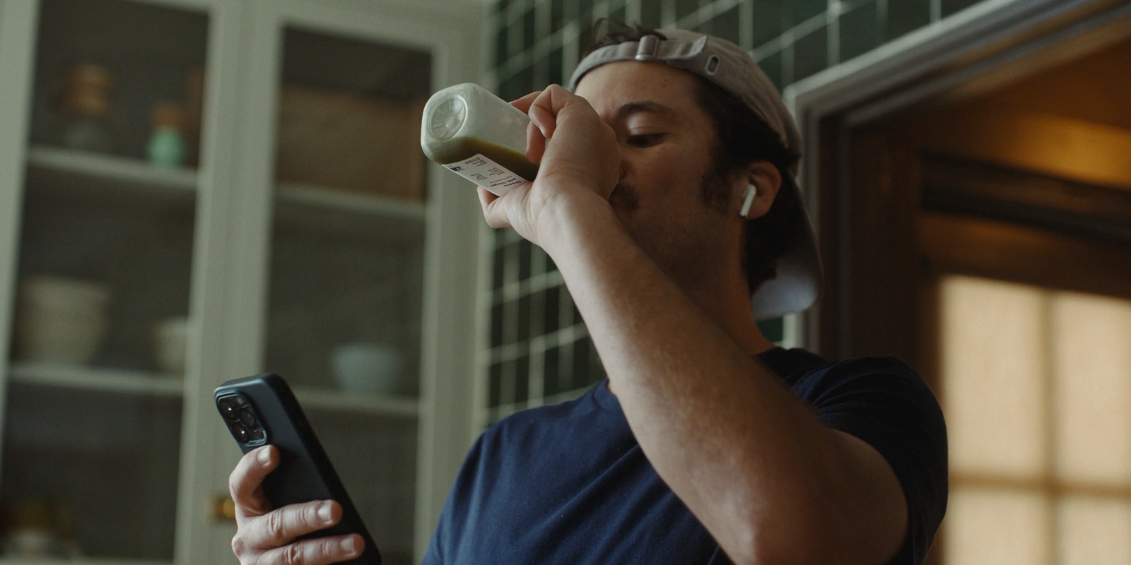 a man drinking from a bottle while holding a cell phone