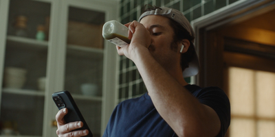 a man drinking from a bottle while holding a cell phone