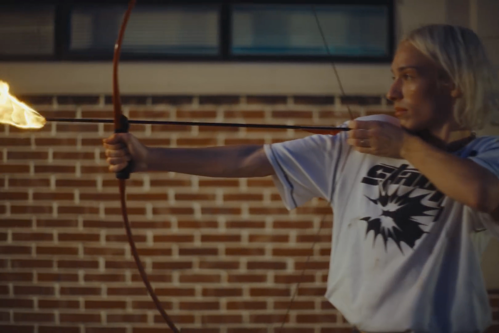 a woman holding a bow and arrow in front of a brick wall