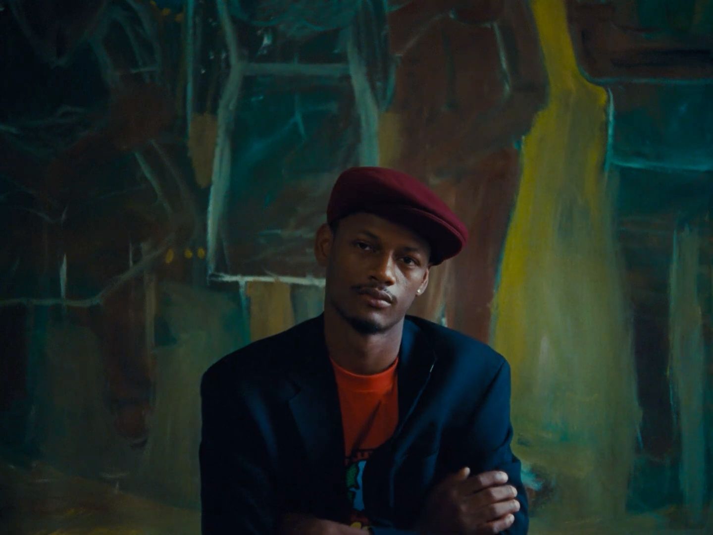 a man sitting in front of a painting wearing a red hat