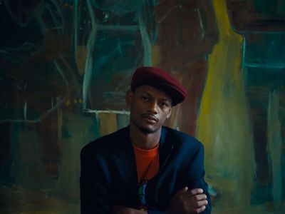 a man sitting in front of a painting wearing a red hat