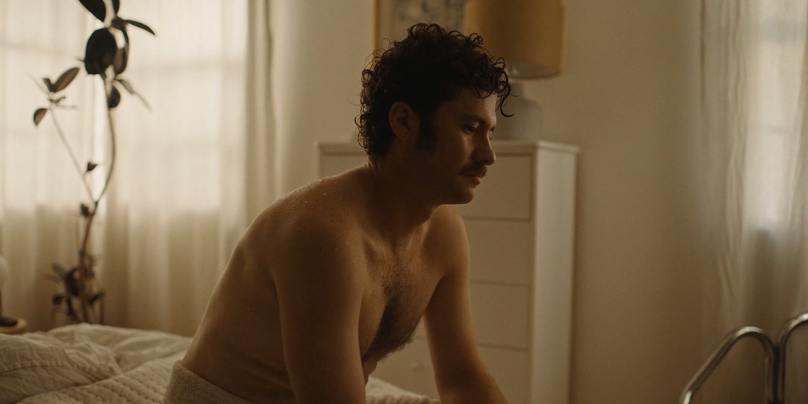 a shirtless man sitting on a bed in a bedroom