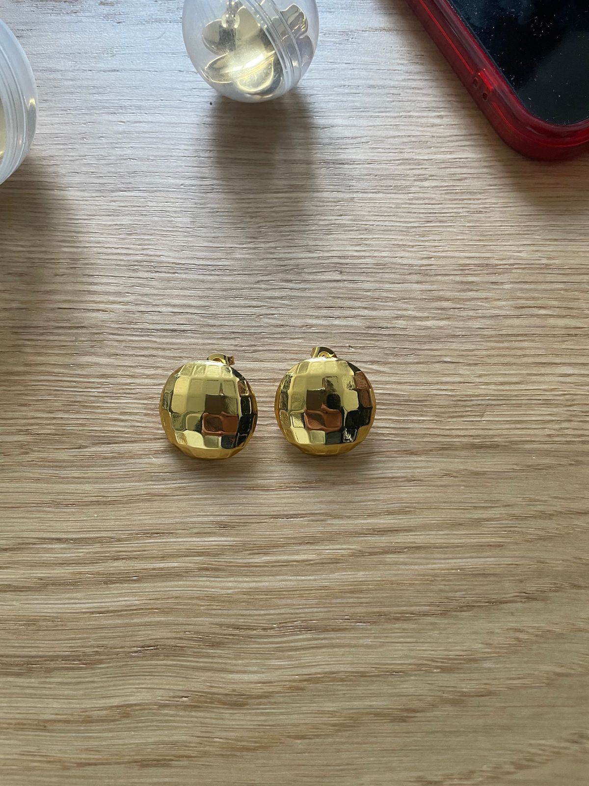 a pair of gold earrings sitting on top of a wooden table