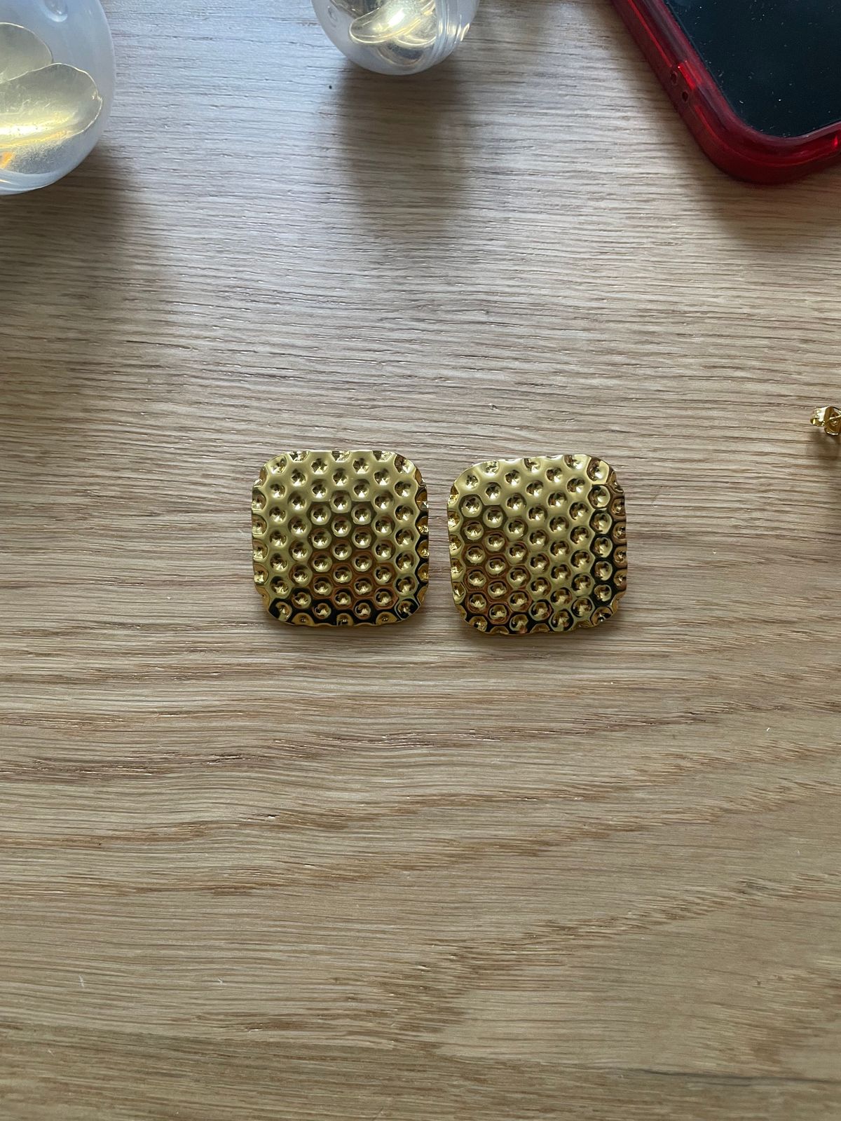 a pair of gold earrings sitting on top of a wooden table