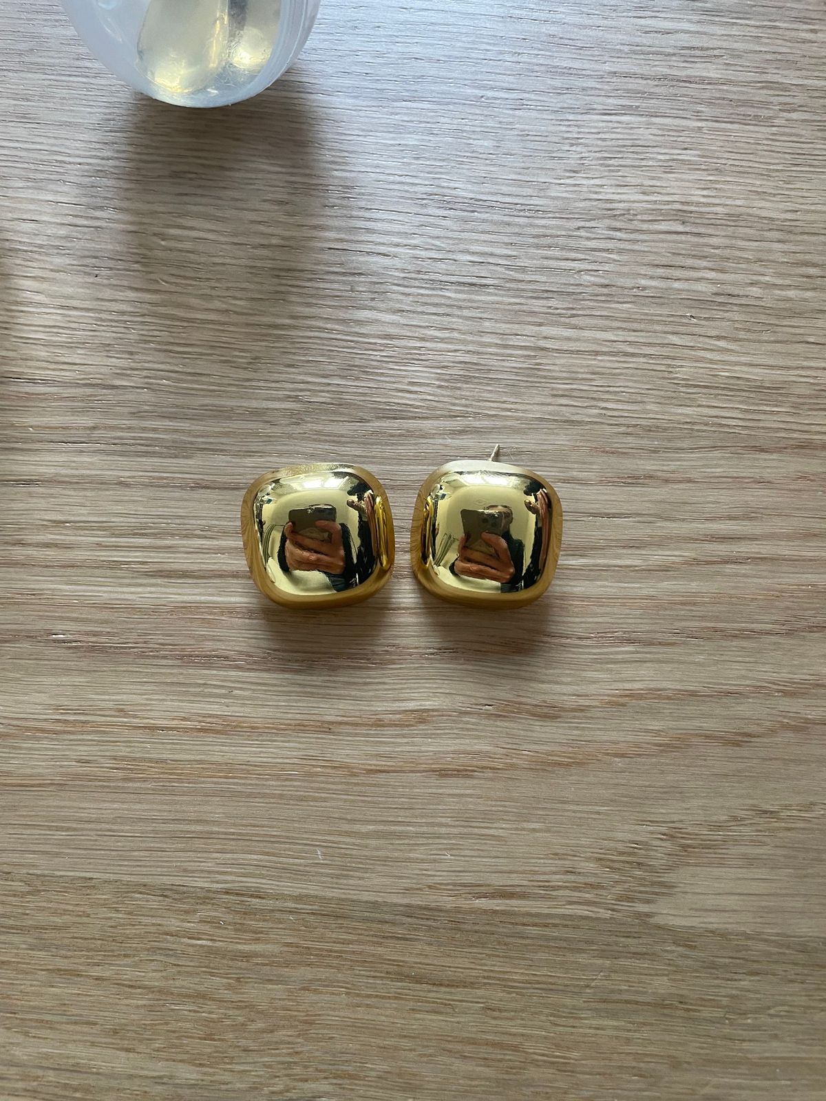 a pair of gold earrings sitting on top of a wooden table