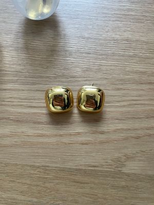a pair of gold earrings sitting on top of a wooden table