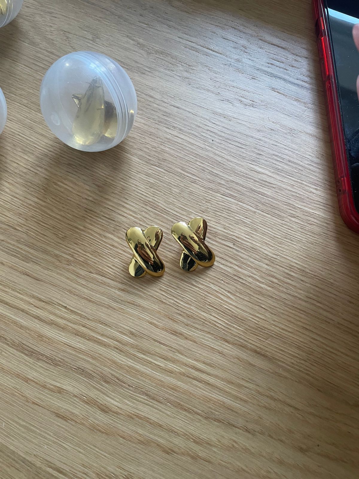 a pair of gold earrings sitting on top of a wooden table