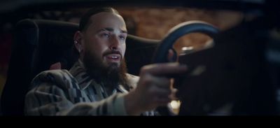 a bearded man driving a car with a steering wheel