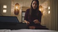 a woman sitting on a bed looking at a laptop