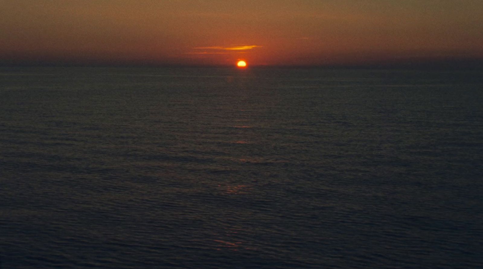 the sun is setting over the ocean on a cloudy day