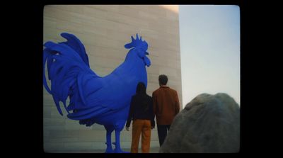 a couple of people standing next to a blue rooster statue