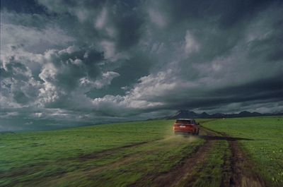 a red truck driving down a dirt road under a cloudy sky