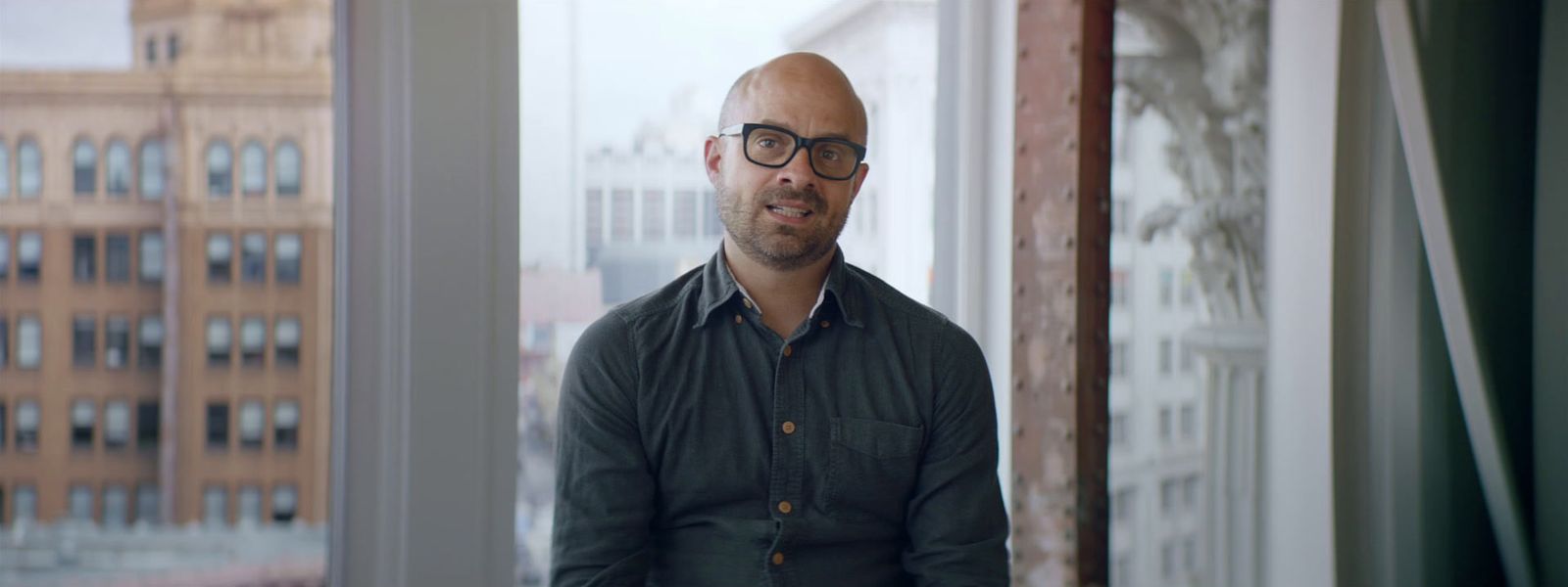 a bald man with glasses standing in front of a window