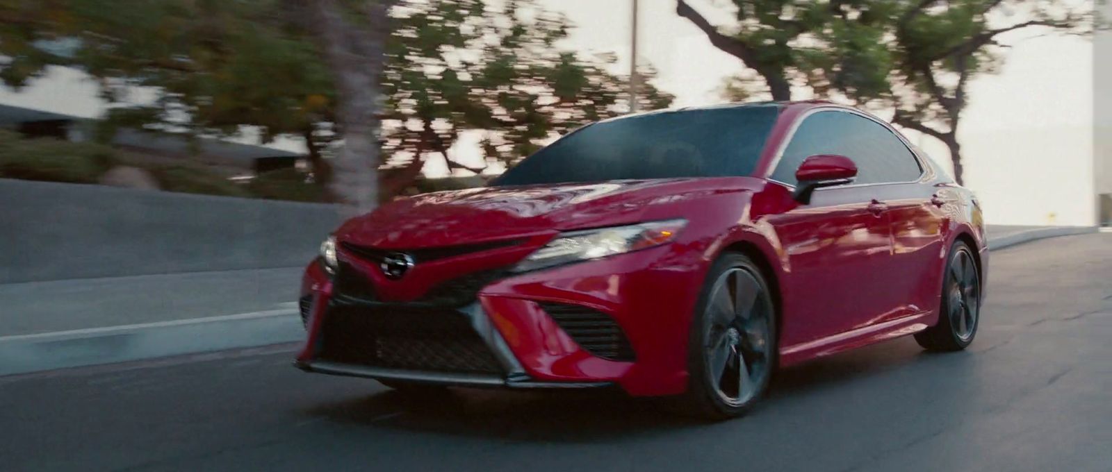 a red car driving down a street next to trees