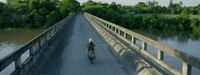 a person riding a bike on a bridge over a river