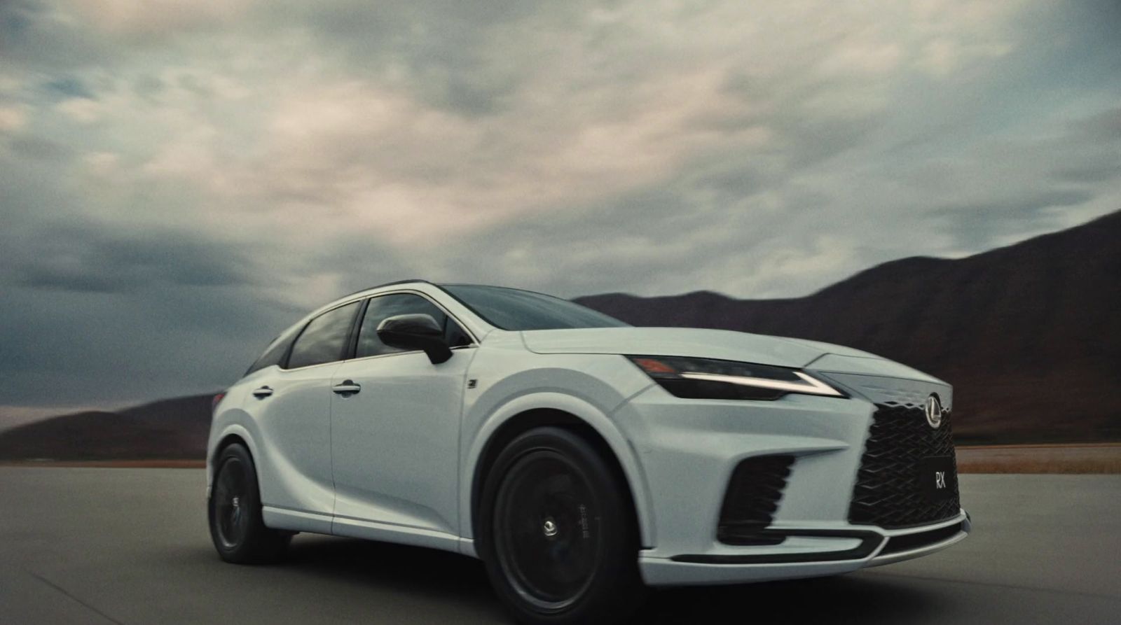 a white car driving down a road under a cloudy sky