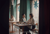 a couple of women sitting at a table in front of a window