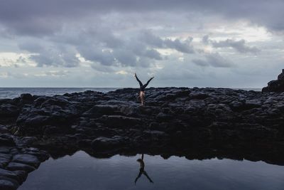 a person standing on a rocky shore with their arms in the air