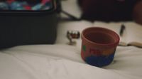 a cup sitting on top of a bed next to an open book