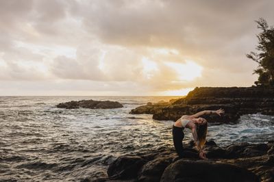 a woman doing a handstand on a rock near the ocean