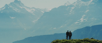 a couple of people standing on top of a lush green hillside