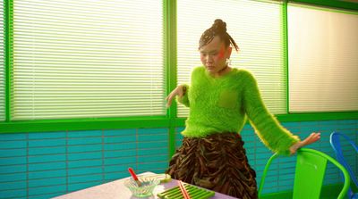 a woman in a green sweater and skirt standing at a table