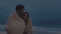 a man and woman wrapped in a blanket on the beach