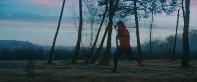 a woman running through a forest at dusk