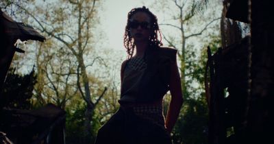 a woman standing in the woods with trees in the background