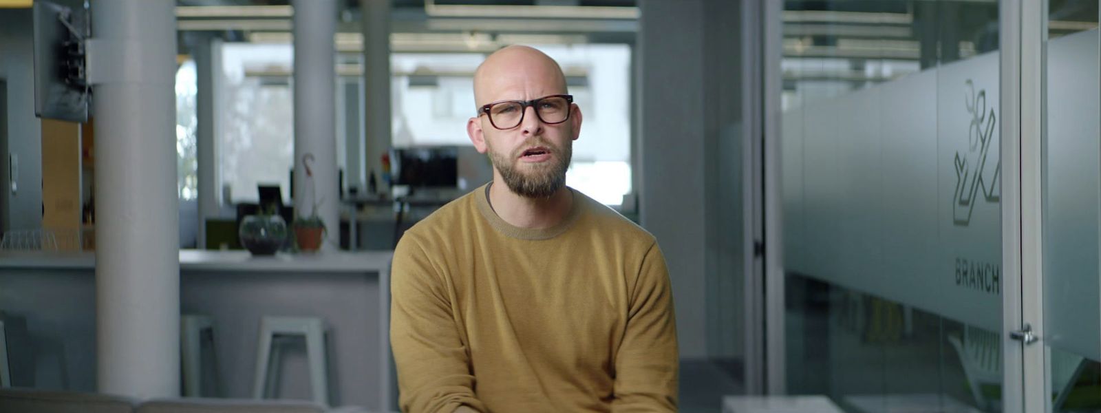 a bald man with glasses sitting in a room