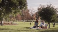 a man and woman sitting on a blanket in a park