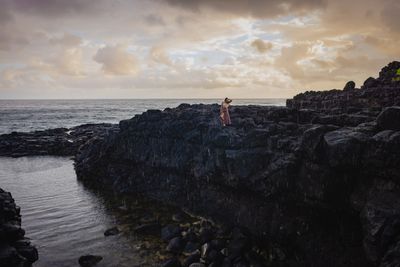 a woman standing on top of a rocky cliff next to the ocean