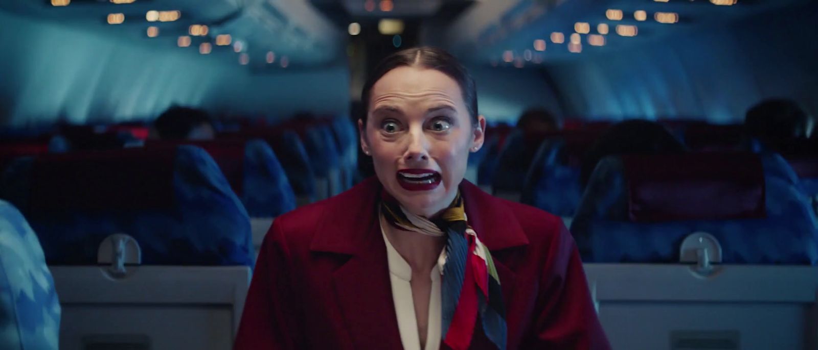 a woman in a red jacket and tie on an airplane