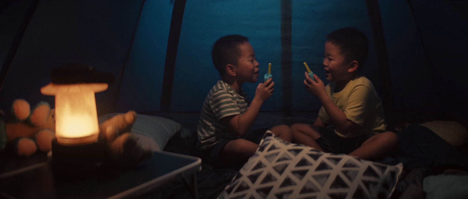 two young boys sitting on a bed in a tent