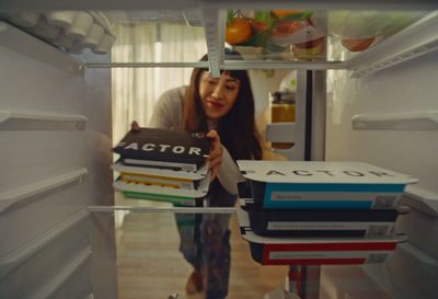 a woman standing in a refrigerator holding a stack of books