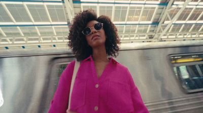 a woman in a pink shirt and sunglasses standing in front of a train