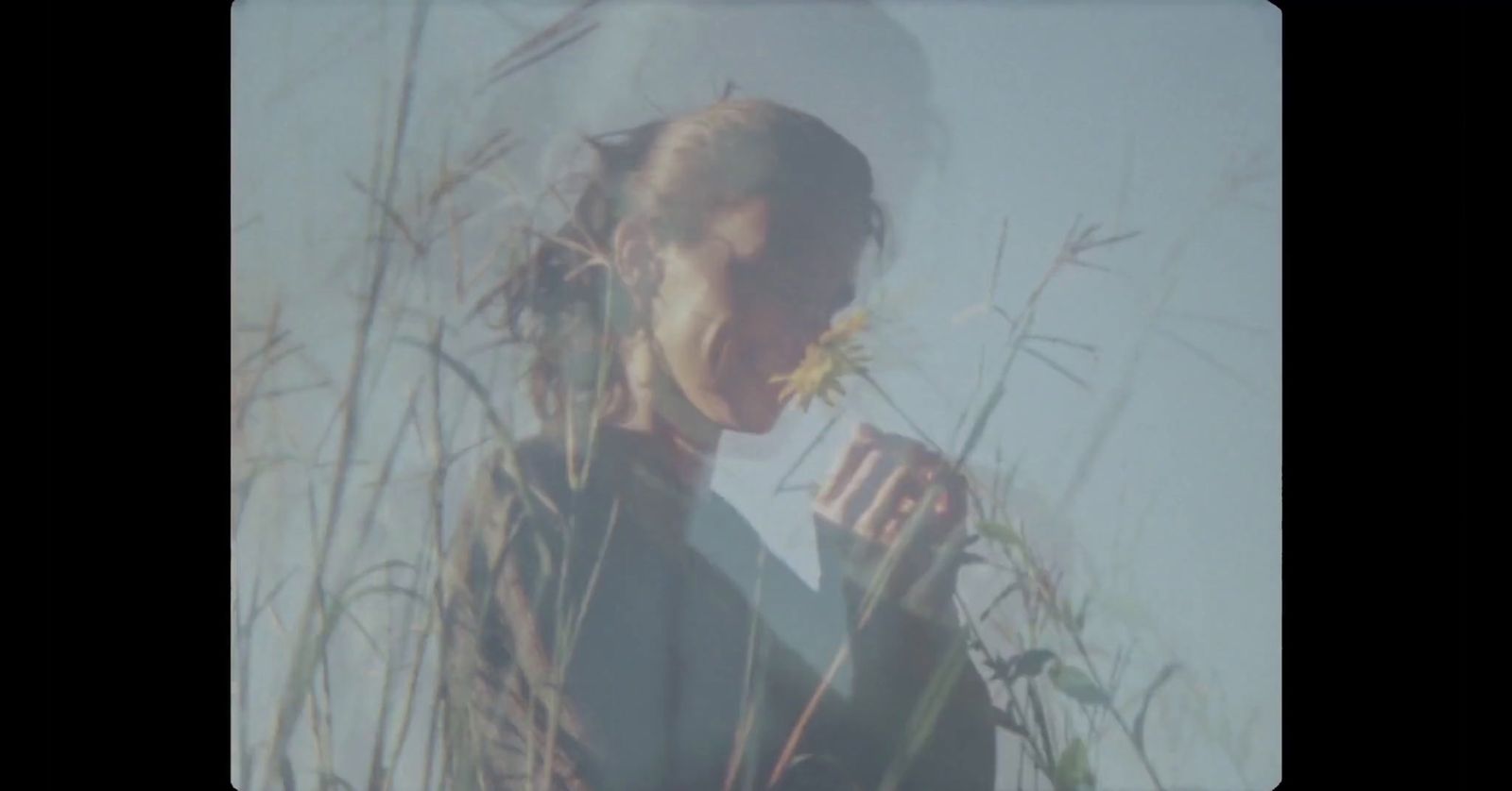 a woman standing in tall grass with a cigarette in her hand