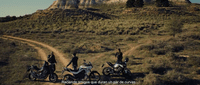 a group of people standing next to motorcycles on a dirt road