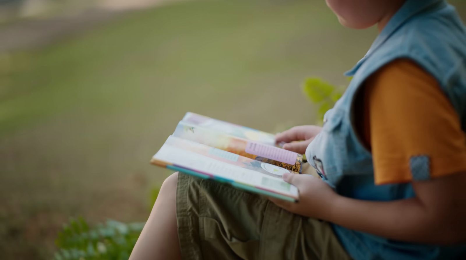 a young boy sitting on a bench reading a book