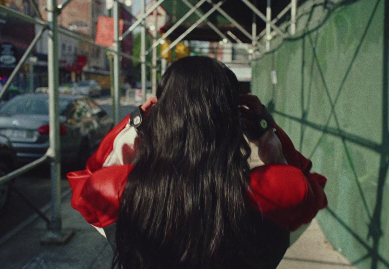 a woman walking down a street next to a green wall