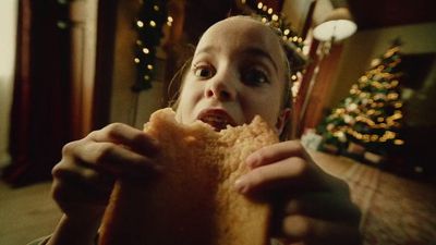 a young girl eating a sandwich in front of a christmas tree