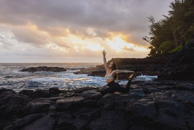 a woman sitting on a rock with her arms in the air