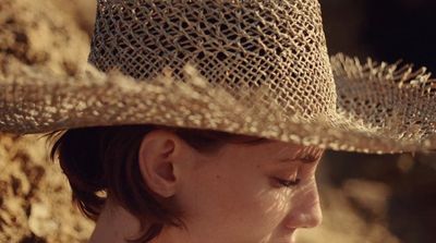 a woman wearing a straw hat and looking off into the distance